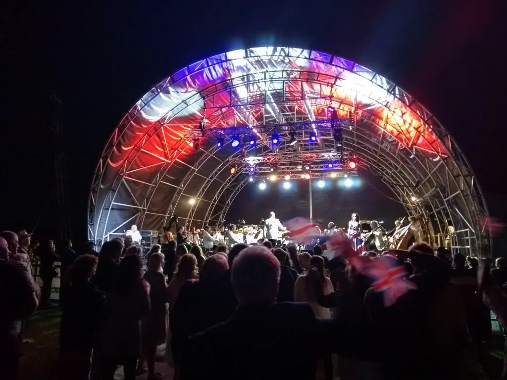 The National Symphony Orchestra playing under a lit shell stage at night, the audience in front of it waving Union flags.