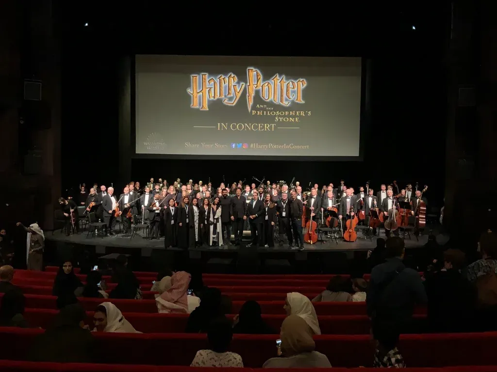 The orchestra taking a bow at Ithra beneath a screen reading Harry Potter and the Philosopher’s Stone in Concert.