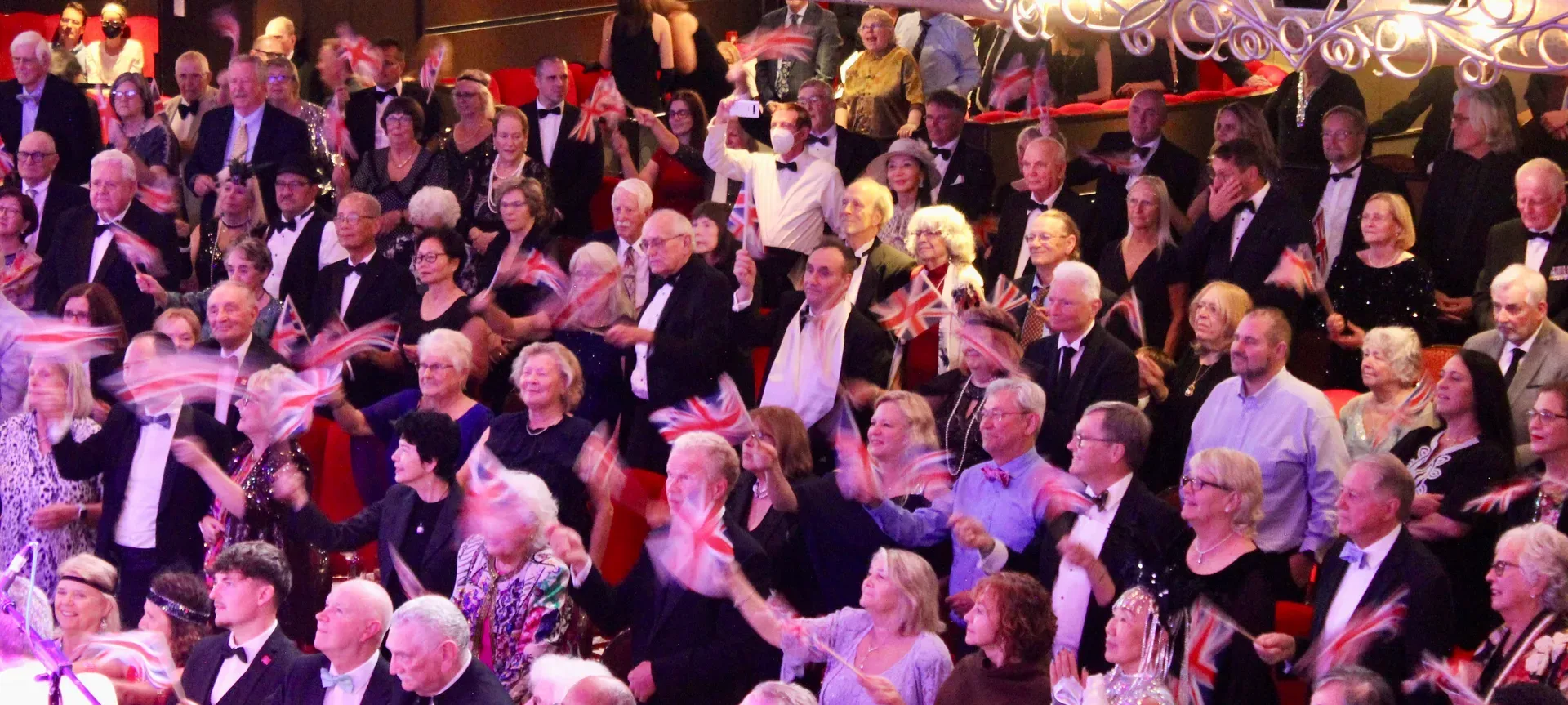 Passengers in evening dress waving Union flags at the Last Night of the Cunard Proms on Queen Mary 2.